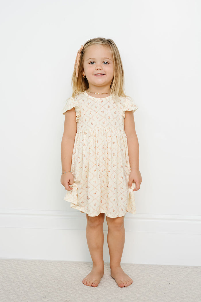 Young girl wearing a yellow dress with ruffled sleeves against a white background