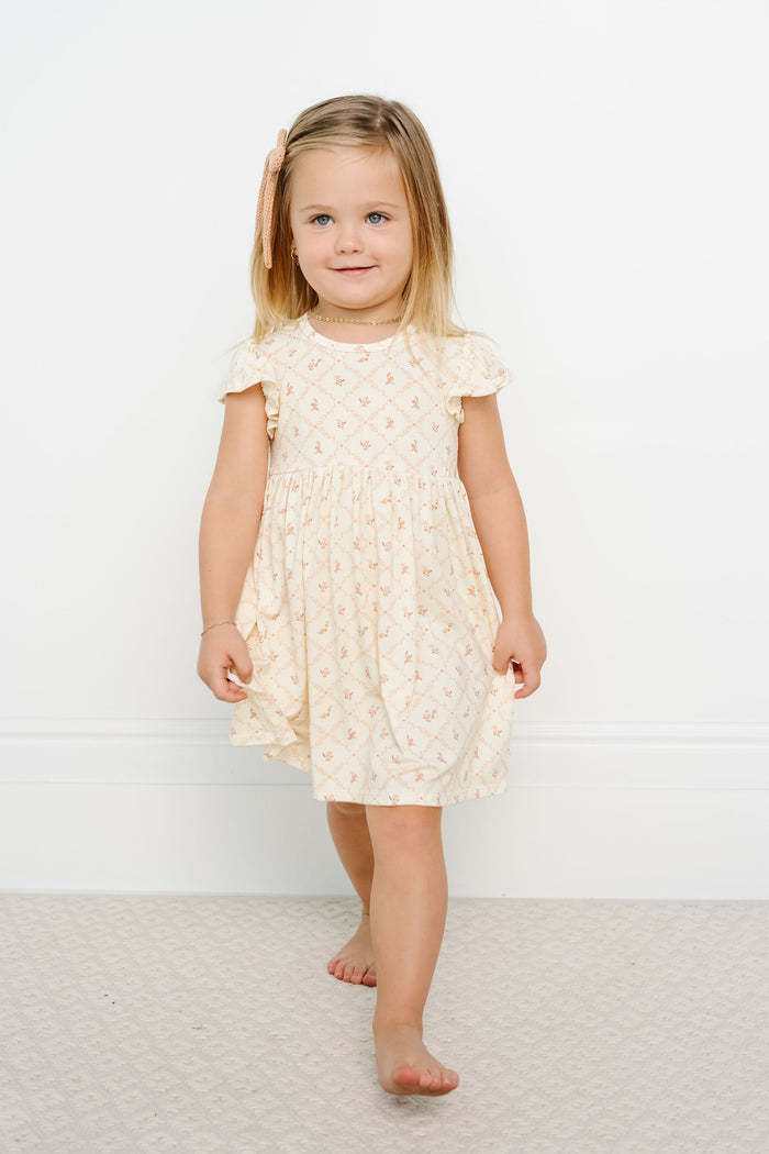 Young girl wearing a cream-colored dress with ruffled sleeves against a white background