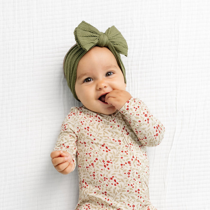 Baby wearing a floral onesie and green headband on a white background