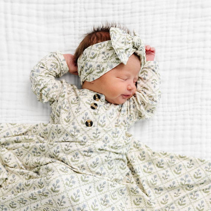 Newborn baby wrapped in a floral patterned blanket with matching headband on a white background