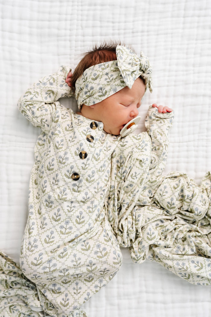 Newborn baby in floral outfit and headband on a white textured blanket