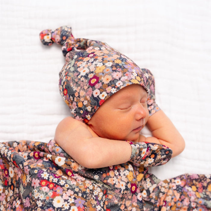 Newborn baby in a floral outfit and hat on a white background